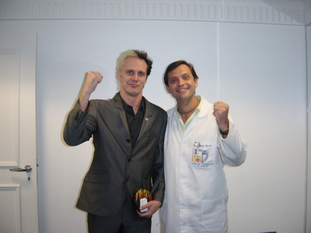 Duas pessoas posando com os punhos erguidos diante de uma parede clara.