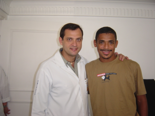 Duas pessoas posando em uma sala de paredes claras.